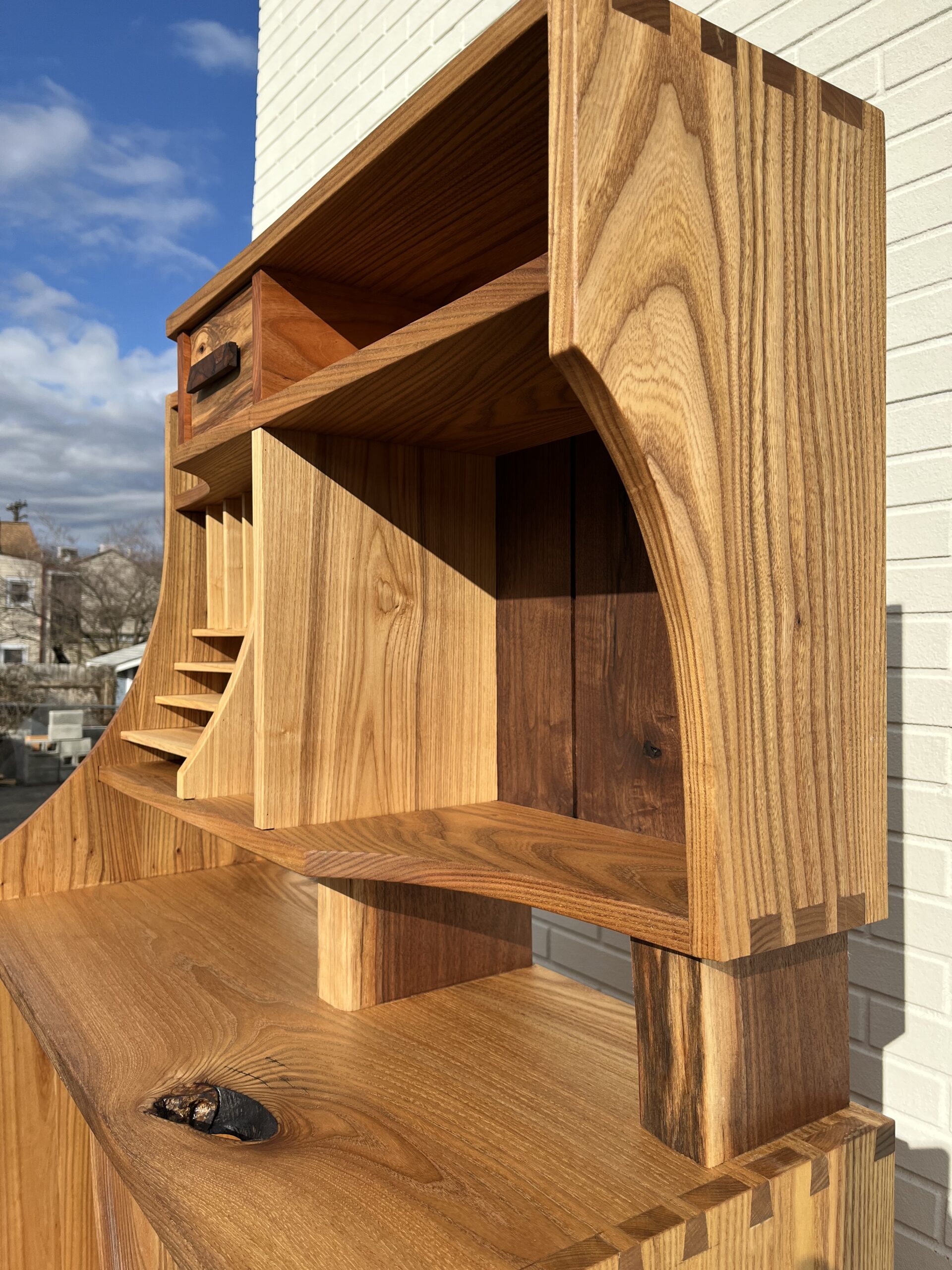 Accents of an entryway cabinet. Upper case of cabinet shows letterbox shelves, drawerface, and four small shelves. Featured wood grain of ash, elm, cherry, and walnut. 45 degree side angle.