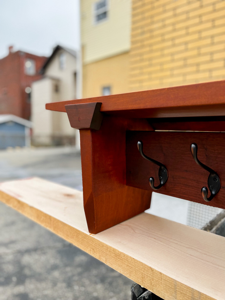 Left end of a coat rack. Details of a keystone accent that joins the top and side of the coat rack are displayed.