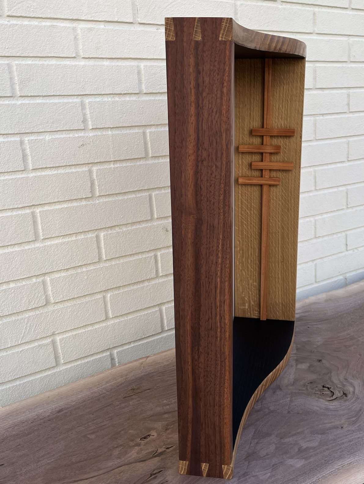 Long walnut side showing pinboard and inside of opposite white oak side of custom frame with cherry inlays. Black stained bottom interior. Frame stands alone on top of walnut slab. Left side vantage. 