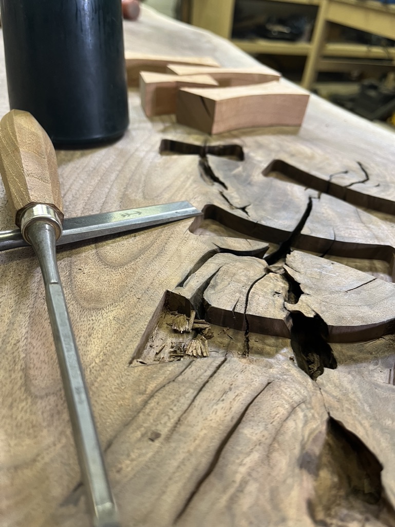 In progress, hand cut dovetails in walnut slab. Hand tools positioned to the left of the dovetails.