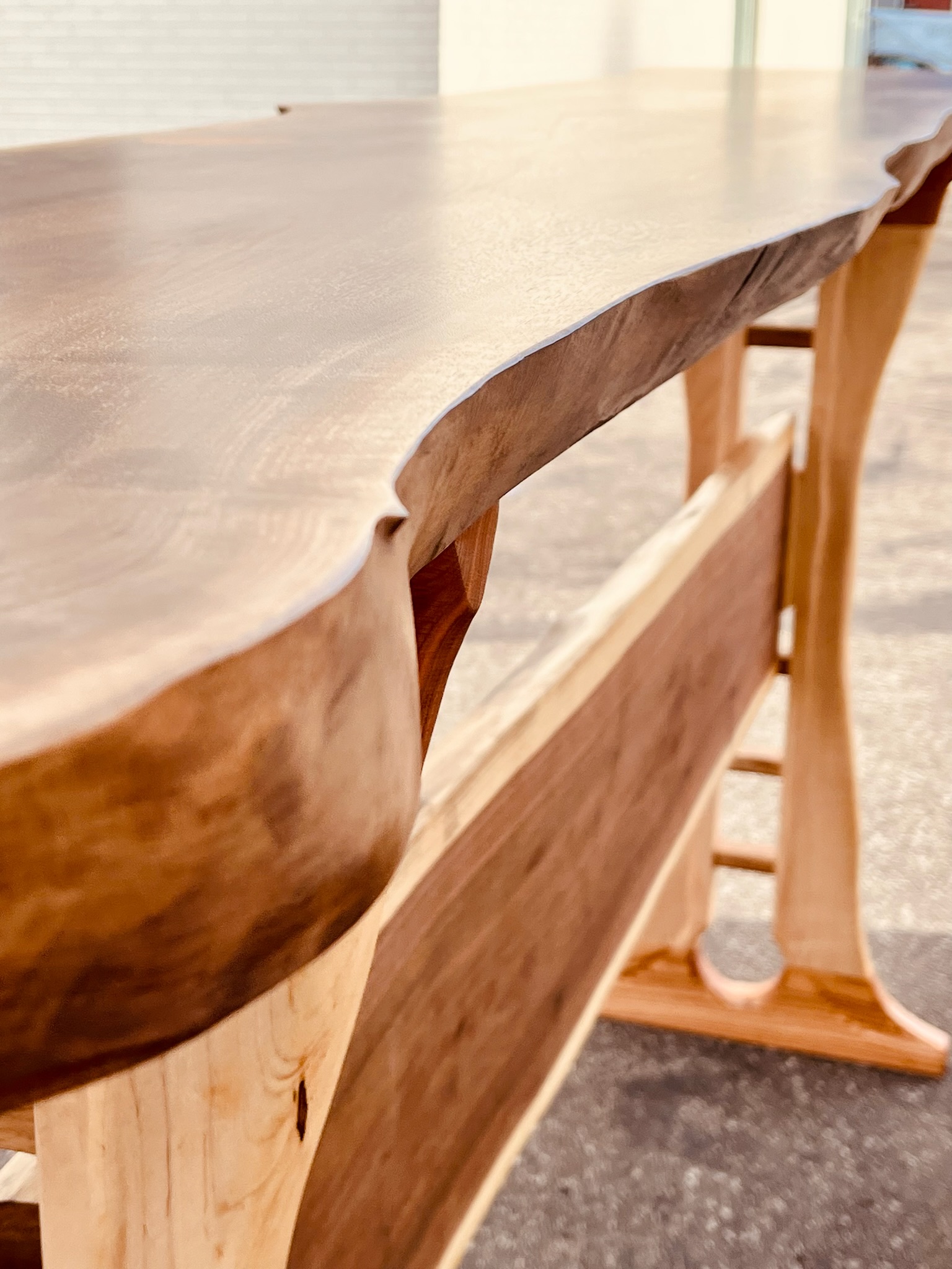 Espresso bar. Trestle style table with maple legs and red oak footers with a walnut tabletop and bridle below. Live edge. Close-up shot. 