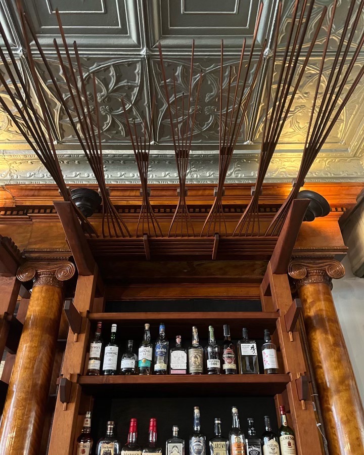 One of the overhead arrays that extend out beyond the bar shelving. Gathered at two points and expanding in a wave-like manner. Overhead lighting showcases their structure and decorative tin ceiling. 