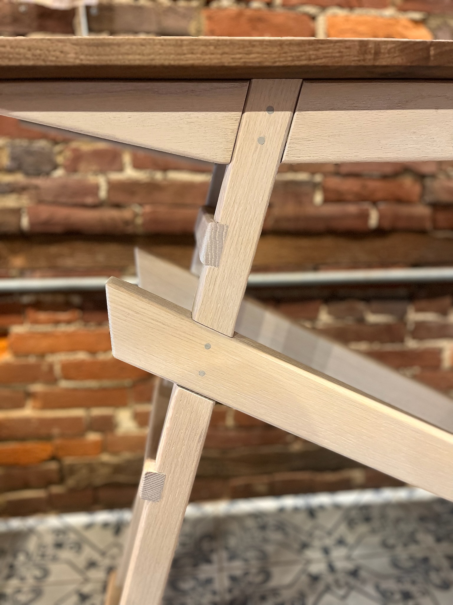 Cross section of display table with beams extending from lower base of legs to the right to the upper legs on the left. Head on view.