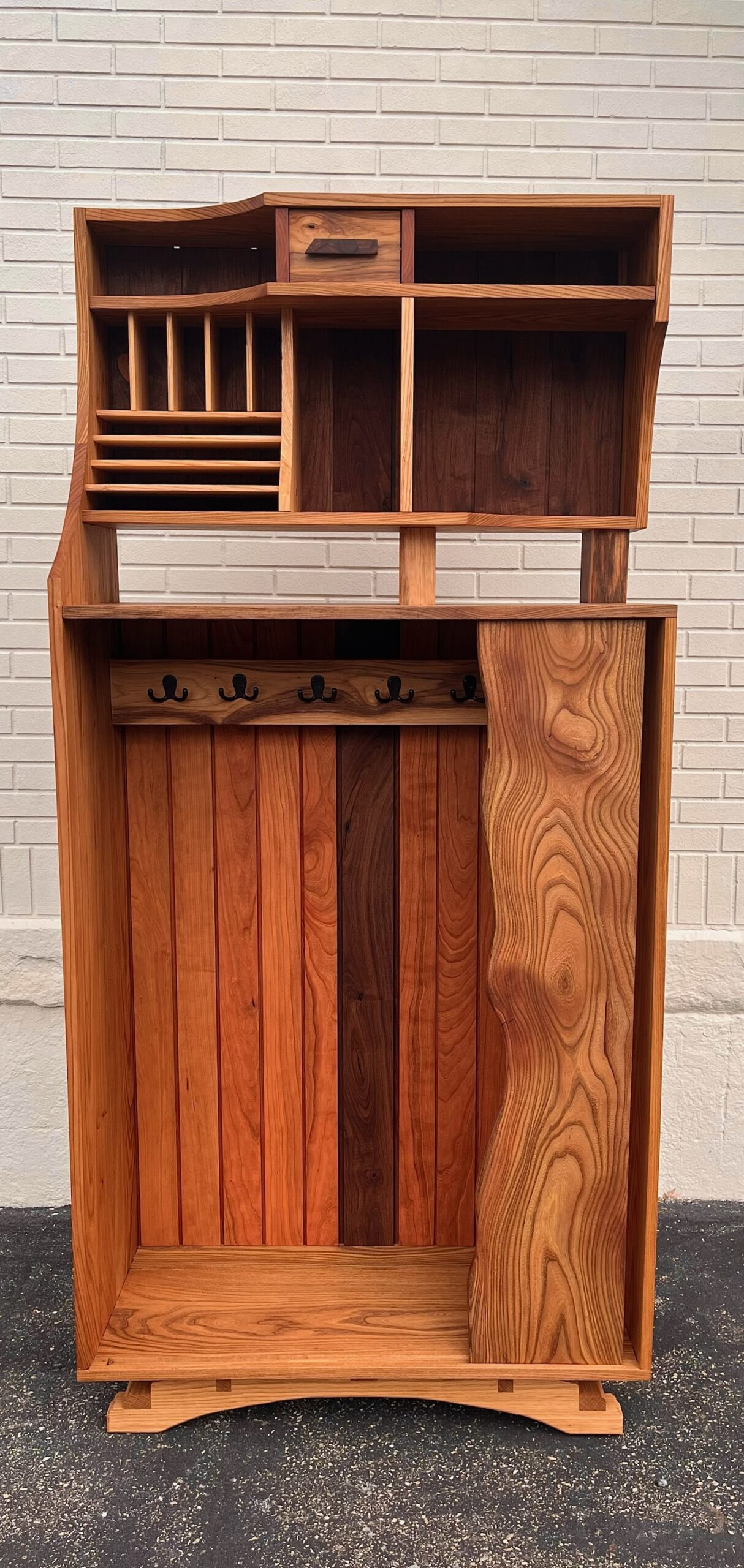 Entrway cabinet. Interior bottom case includes a coat rack. Upper case includes a letterbox and uniquely designed storage and open-shelf compartments. Made from visibly various wood species: elm, cherry, walnut, spalted maple, and ash. Sliding door contains vivid swirling woodgrain. Paneling back made from cherry with a walnut center board. 