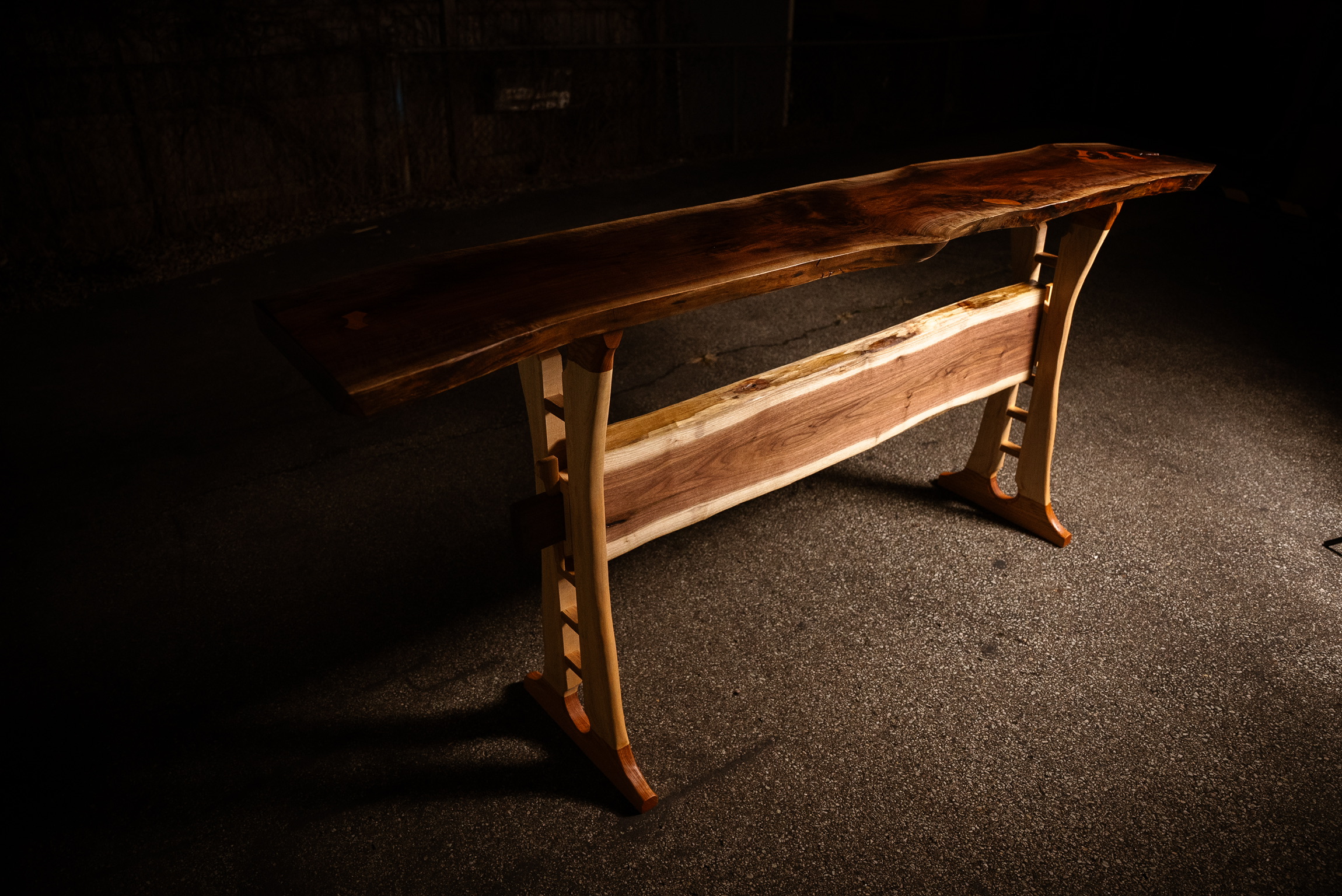 Standing bar; sapwood and walnut bridle prominently featured, shadows of decorative accents on the maple legs. Moody, dark photograph. 