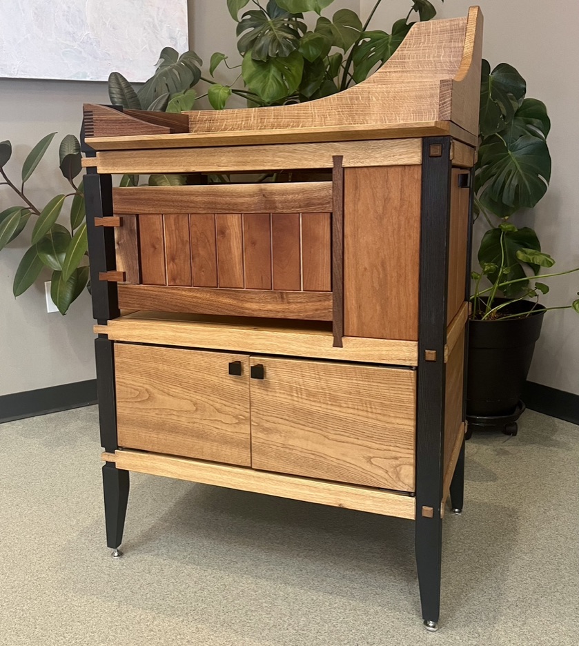 Kitchen server station. Top portion is made from white oak with undulating curves that come to a landing on the right side. Finger joints featured in front of top. Bblack stained, ash legs surround the piece with interlocking mortise and tenons prominently featured. Center portion contains floating cherry and walnut panel to cloak empty space. Sliding dovetails in cherry and walnut. Cherry storage cabinet on right side. Bottom storage space comprised of white walnut with matching grain that waterfalls around the piece. 