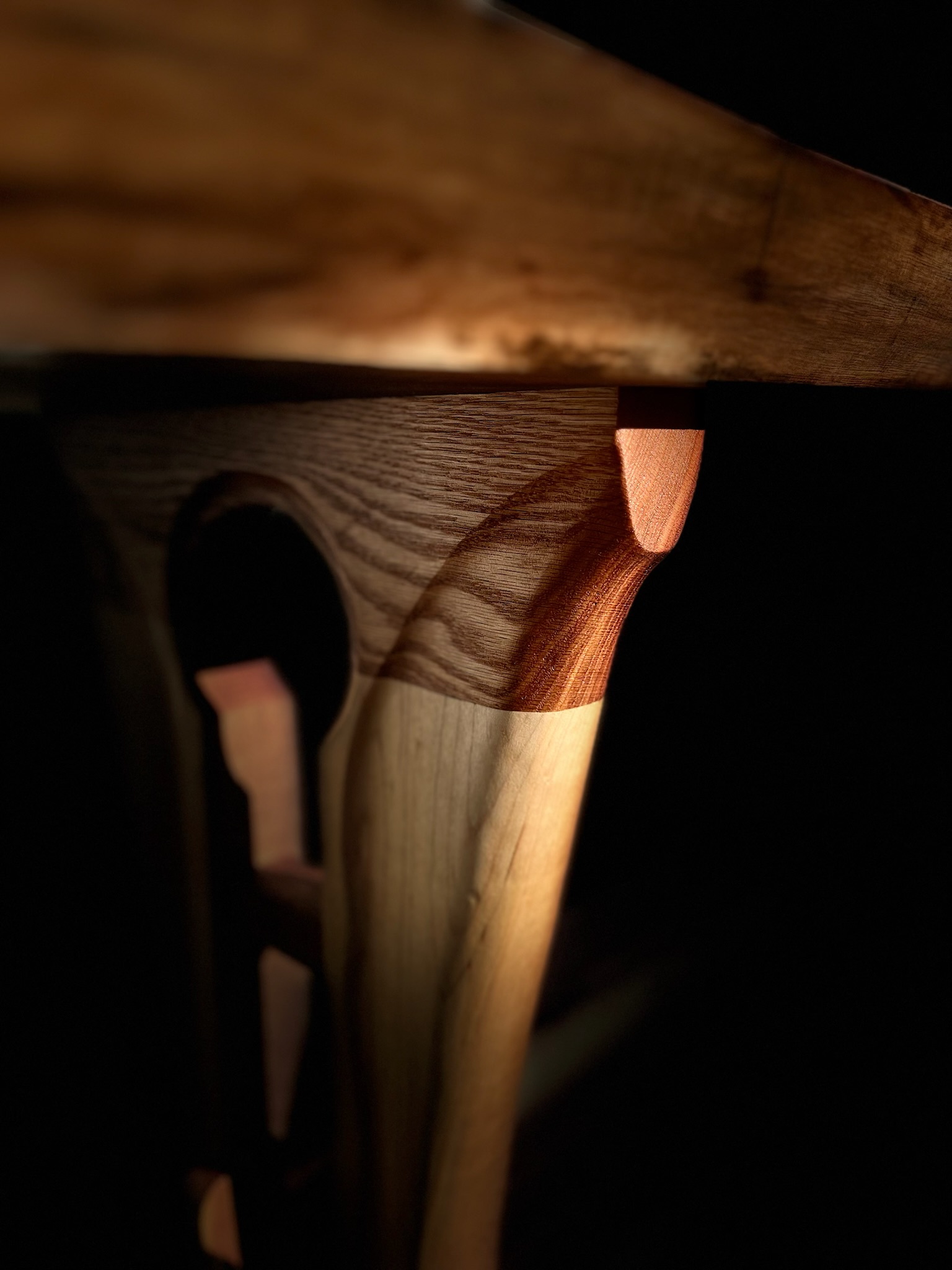 Tabletop underside, top of table leg; highlighting the profile of the handcarving in the legs with red oak and maple species. 