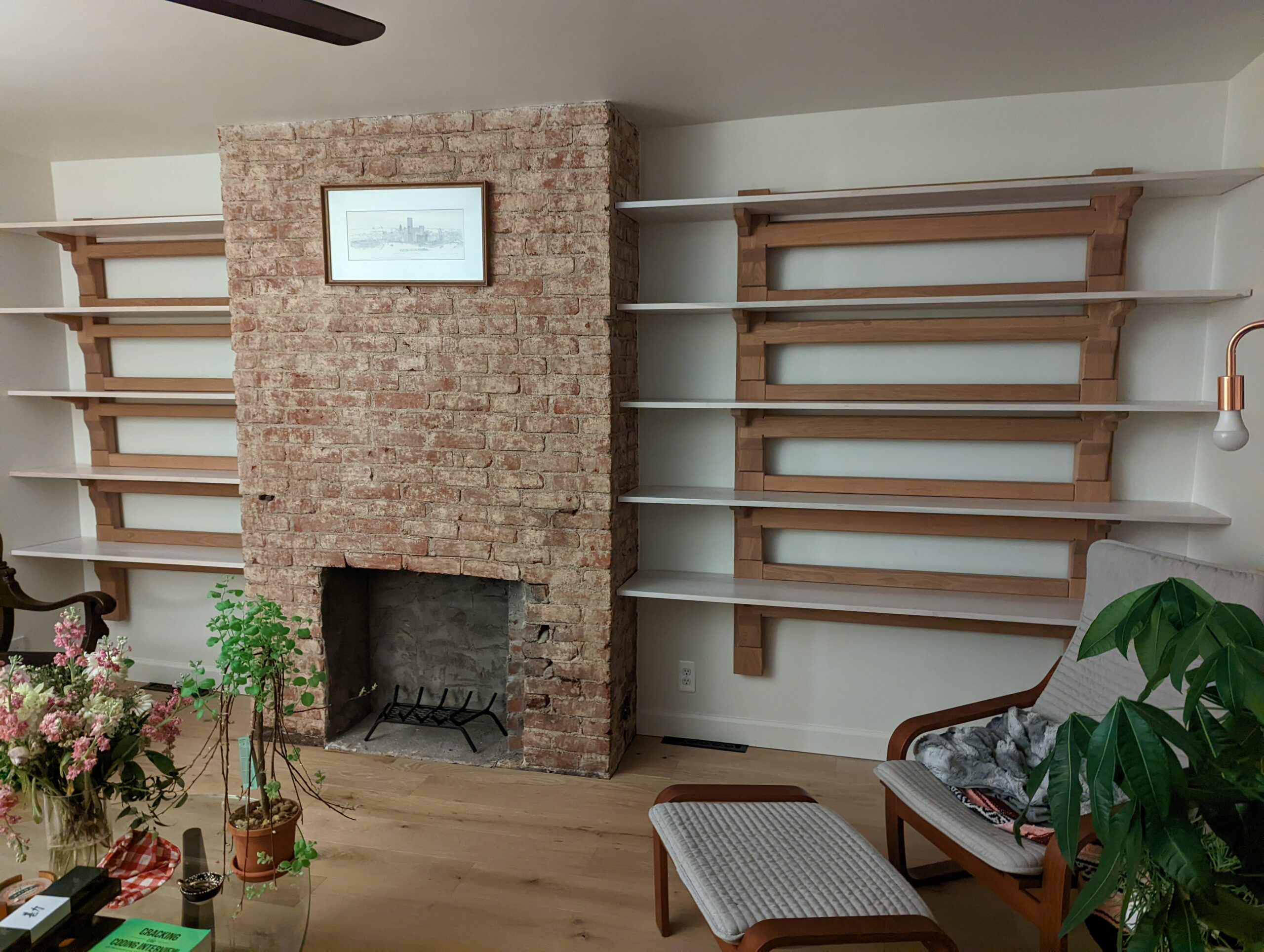 Shelving structure hung on white wall. Shelving made from white oak using traditional Japanese joinery. Panned out image of two shelving units surrounding a fireplace.