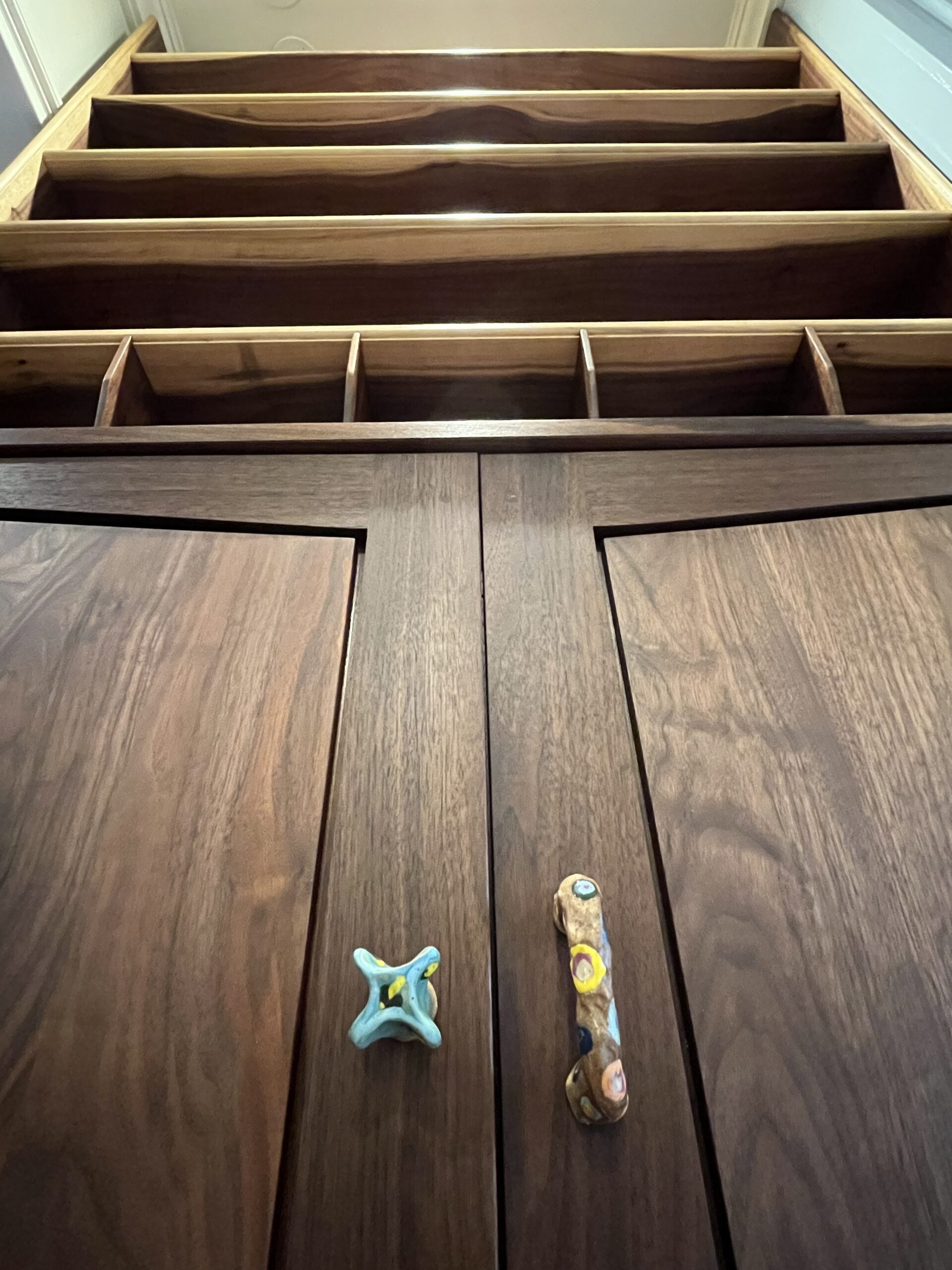 walnut cabinet and overhead shelving, looking up front the floor and focused on custom ceramic handpull and handle.