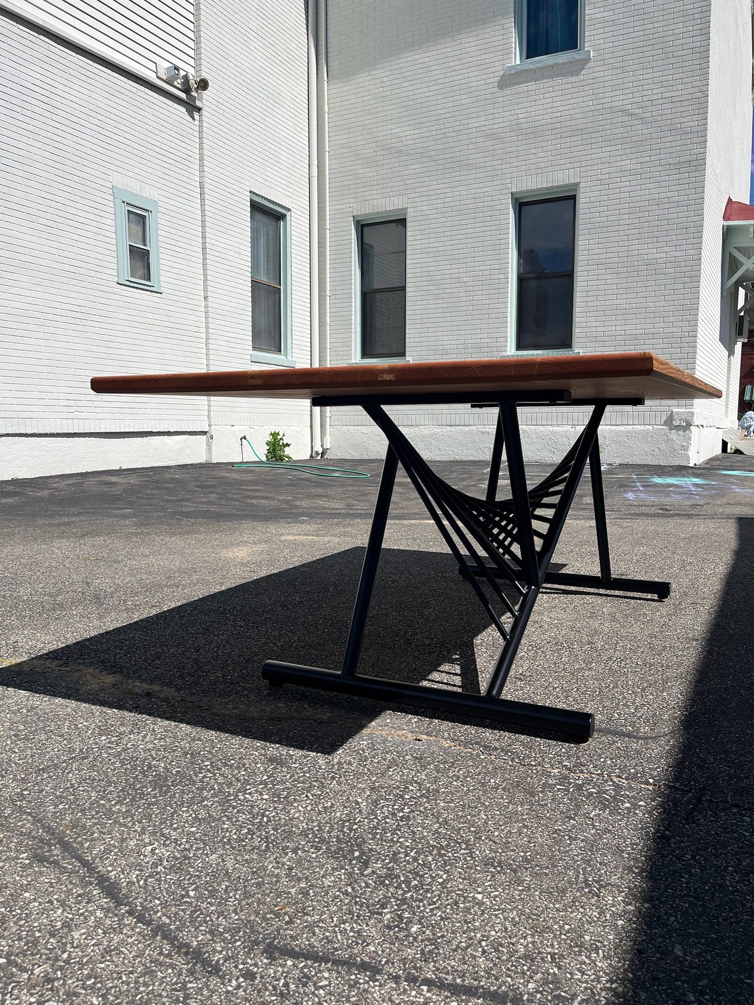 White brick house as a backdrop displaying the underside of a Red Oak table top and base. Displaying the unique curvature of the black steel base.